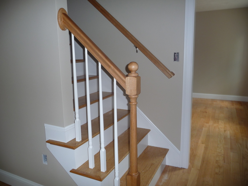 Wooden staircase with white spindles and a tan wall, leading up from a hardwood floor.