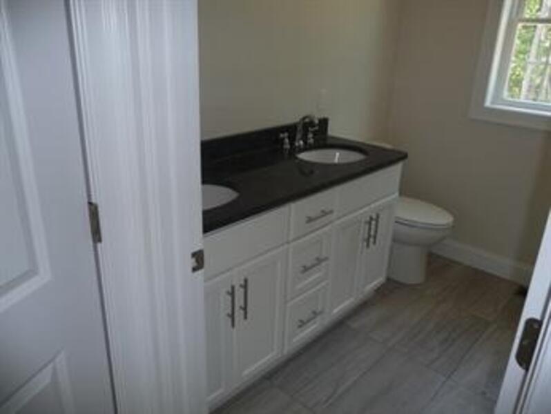 Bathroom with double sink vanity, black countertop, and toilet near a window.