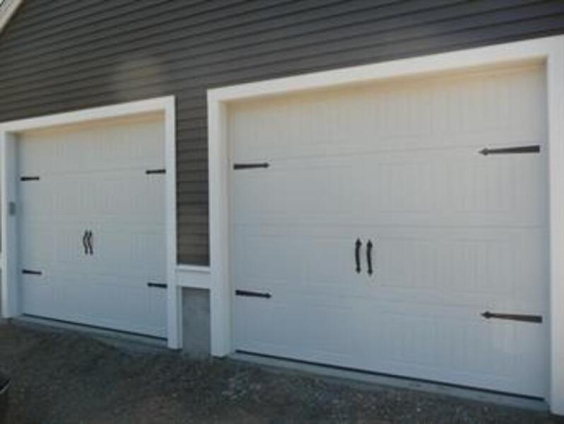 Two white garage doors with black handles and hardware on a dark-sided building.