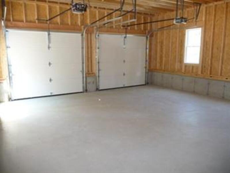 Empty two-car garage with unfinished wood walls, concrete floor, and two closed doors.