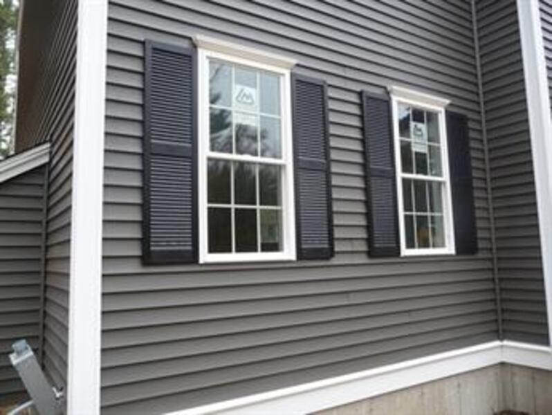 Gray house siding with two windows, each framed by black shutters and white trim.