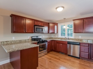 Modern kitchen with wood cabinets, granite countertops, stainless appliances, and wood floors.