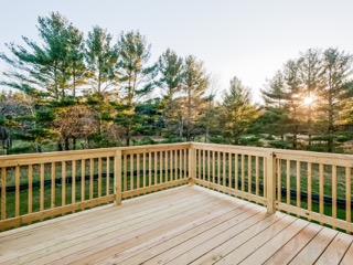 Wooden deck with railing overlooks grassy yard and tall pine trees at sunset.