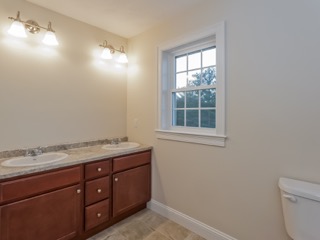 Bathroom with double sinks, wooden cabinets, a window, and toilet on the right.