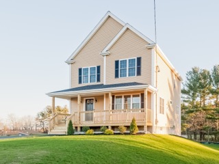 Two-story beige house with a front porch and green lawn on a clear day.