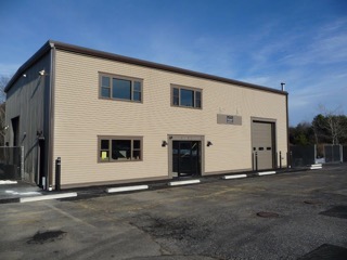A beige, two-story industrial building with large windows and a garage door.