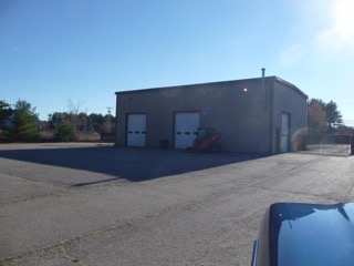A small metal garage with two large doors and a tractor parked outside on a sunny day.