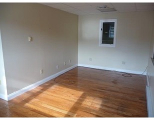 Empty room with beige walls, a window, and sunlight reflecting on hardwood floors.