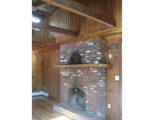 Brick fireplace with wooden mantel in a wood-paneled room with exposed ceiling beams.