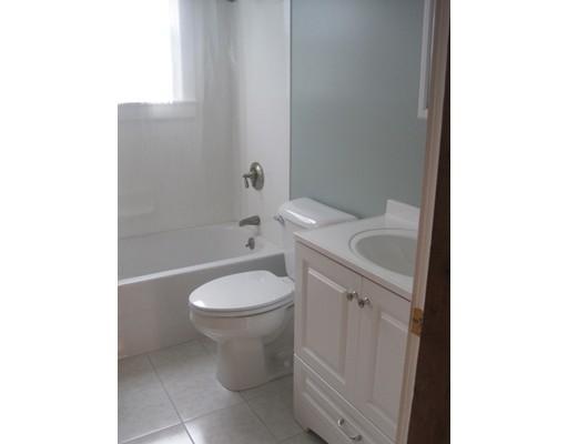 Small bathroom with a white bathtub, toilet, and sink vanity next to a window.