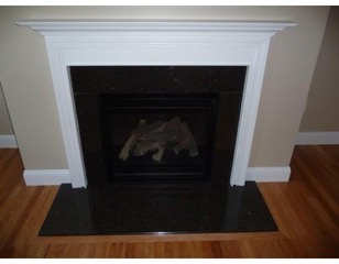 A black fireplace with a white mantel on a hardwood floor against a beige wall.