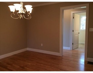 Empty room with hardwood floors, beige walls, and a ceiling light fixture near an open doorway.