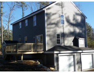 Two-story gray house with a wooden deck and double white garage doors.