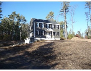 Two-story gray house with white trim on a bare dirt lot, surrounded by tall trees.
