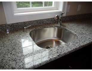 Granite countertop with a stainless steel sink and faucet below a window.