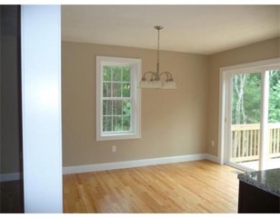 Empty dining area with wooden floor, window, chandelier, and sliding glass door to a deck.