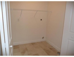 Empty laundry room with beige tile floor, white walls, and a wire shelf on the back wall.