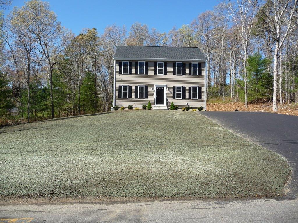 Two-story beige house with black shutters, driveway, and newly seeded front lawn.
