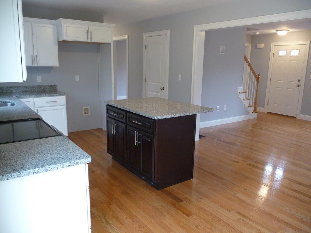 Modern kitchen with wooden floors, granite countertops, and a central island near entryway.