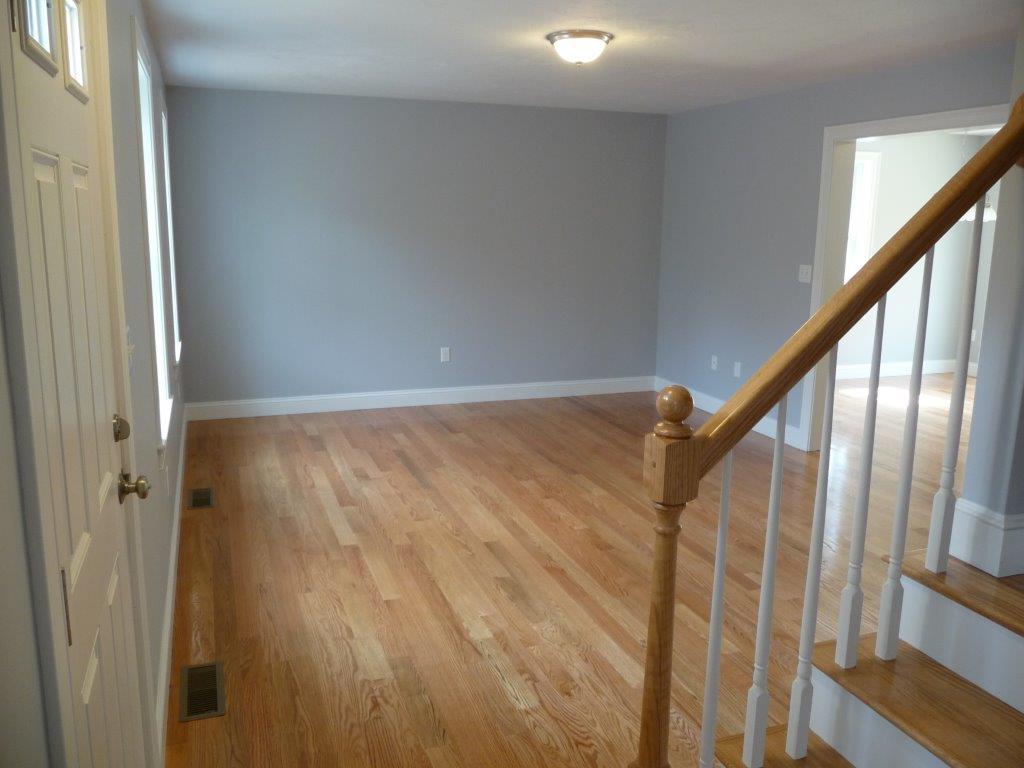 Empty room with light wood flooring, gray walls, and a staircase with a wooden banister.