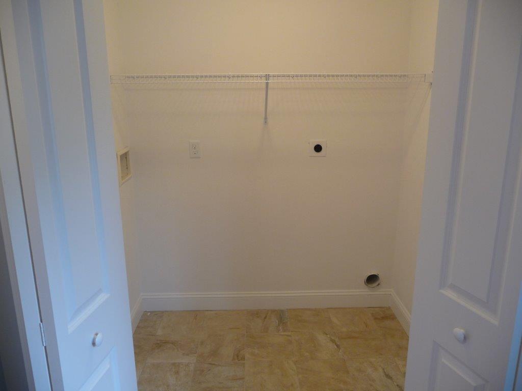 Empty laundry room with tiled floor, white walls, and a single wire shelf on the back wall.