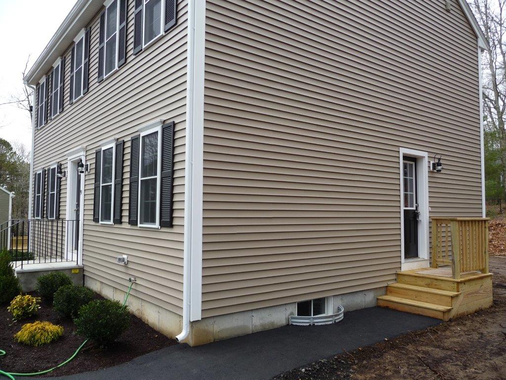 Two-story beige house with black shutters, small wooden porch, and landscaped yard.