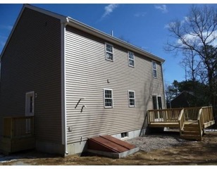 Beige two-story house with a wooden deck and bulkhead doors on the side, under blue sky.