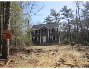 A two-story house stands at the end of a dirt driveway surrounded by trees and woods.