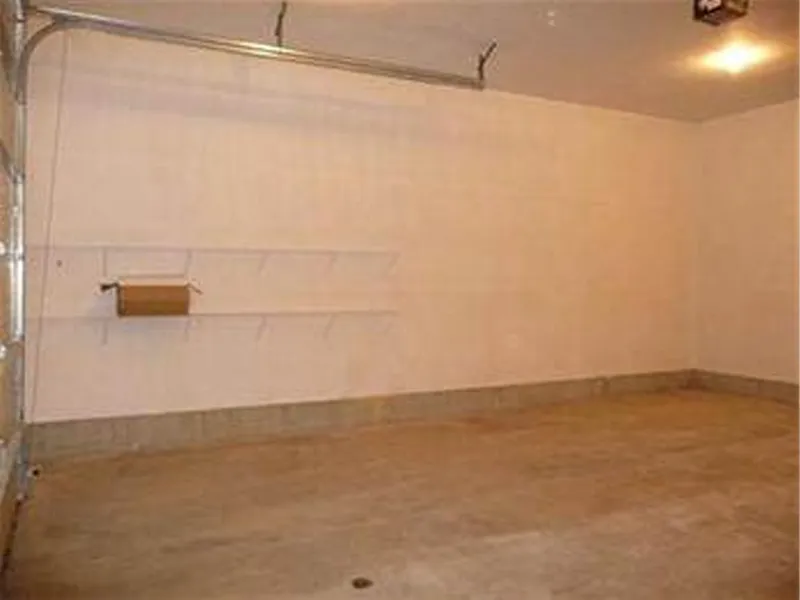 Empty garage with bare walls, shelves, and a single light on the ceiling.