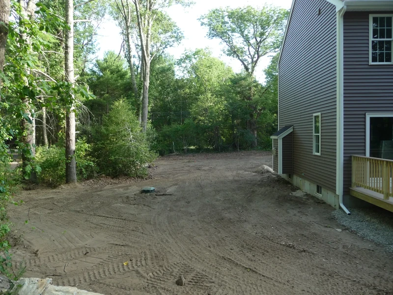 A cleared, dirt yard next to a house with trees and greenery in the background.