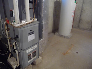 A furnace and water heater installed in a basement with concrete walls and floor.