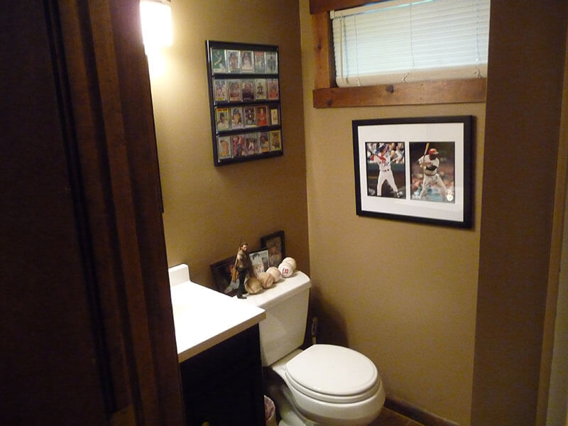 Small bathroom with tan walls, framed sports photos, and a white toilet under a window.