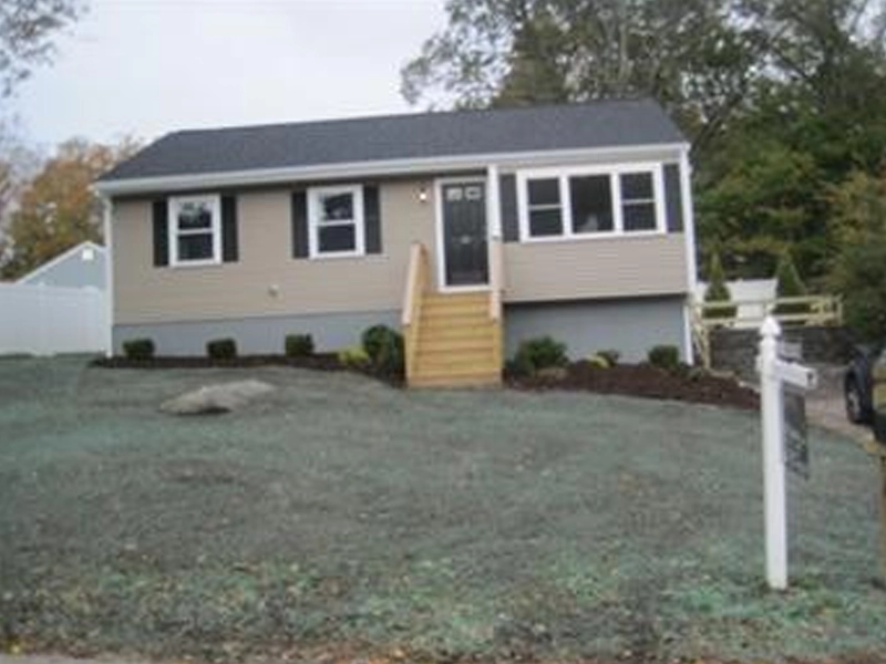 Single-story beige house with steps leading to front door, set on a grassy, sloped yard.