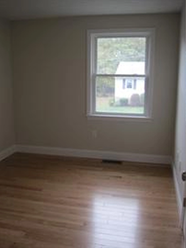 Empty room with light-colored walls, wood floor, and a window showing a house outside.