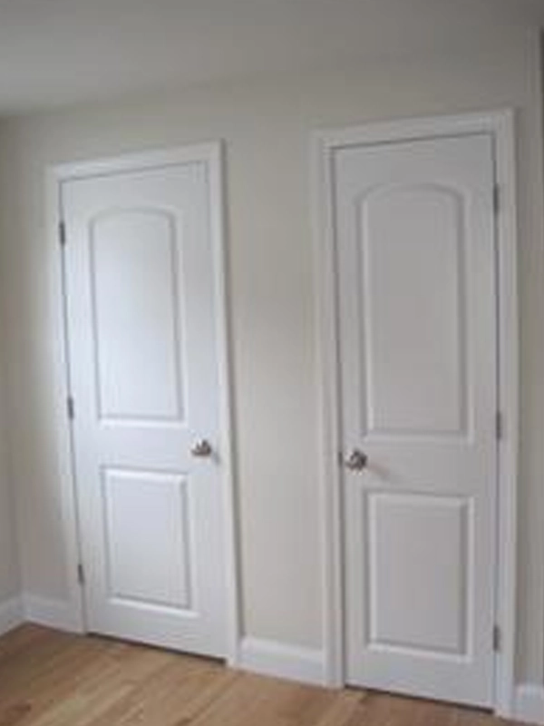 Two white interior doors side by side in a beige room with wooden flooring.