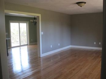 Empty room with hardwood floors, gray walls, and a view into a dining area with sliding doors.