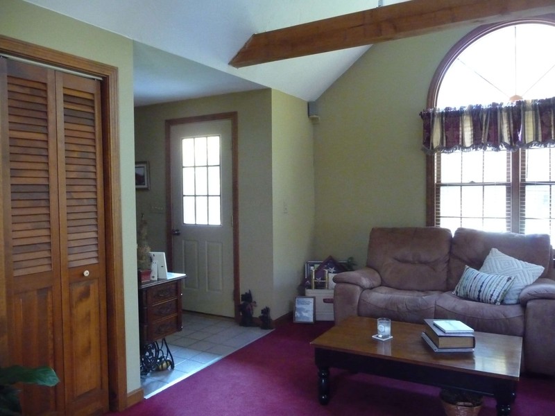 Living room with beige couch, wooden coffee table, and door near large window with curtains.