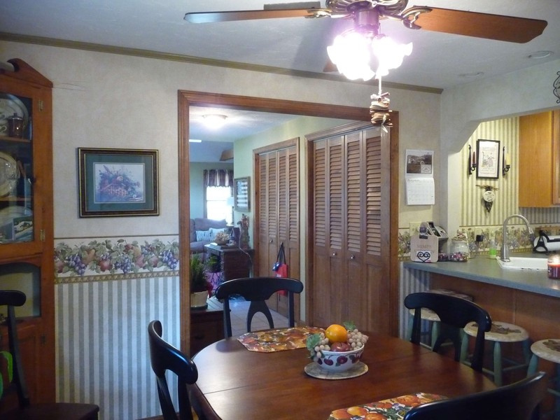 A cozy dining room with a wooden table, chairs, and floral wallpaper near a kitchen.
