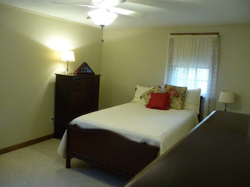 Bedroom with a bed, dresser, nightstand, lamp, and window with sheer curtains.