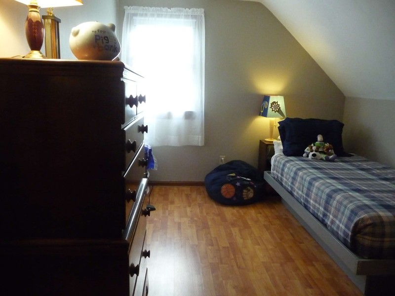 A neatly made bed in a cozy bedroom with wood floors and a chest of drawers.