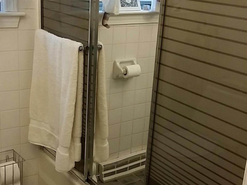 White towel on glass shower door in bathroom with tile walls and a roll of toilet paper.