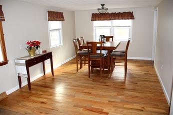 Dining room with wooden floor, table, six chairs, console table, and two windows.