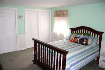 Bedroom with a wooden bed, striped bedding, stuffed animals, and closed white closet doors.