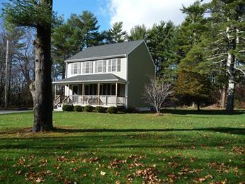 Two-story house with a front porch, surrounded by trees and a large grassy yard.