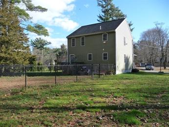 Two-story house with a fenced backyard and scattered trees under a partly cloudy sky.