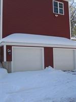 Snow covers the ground in front of a red house with two white garage doors.