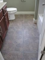A small bathroom with gray tile floor, a toilet, vanity, and bathtub.