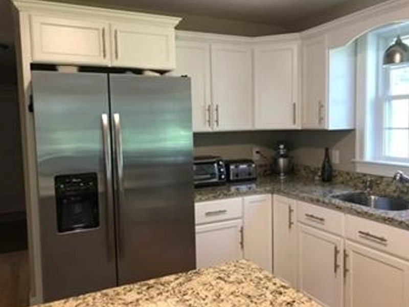 Modern kitchen with stainless steel fridge, granite counters, white cabinets, and small appliances.