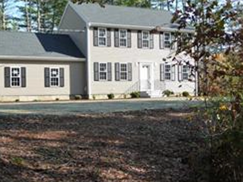Two-story beige house with black shutters and attached garage, surrounded by trees.