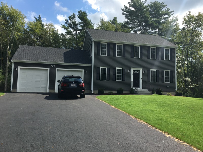Two-story gray house with black shutters, double garage, and a black car in the driveway.